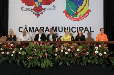 Mesa Diretora composta pela Defensora Pública e Presidente do Conselho Municipal dos Direitos da Mulher, Ana Flávia Diniz; Prefeito Municipal de Viçosa, Raimundo Nonato Cardoso; Vice Reitora da Universidade Federal de Viçosa, Rejane Nascentes e a representante do 3º Pelotão do Corpo de Bombeiros Militar de Viçosa, Cabo Kalina Lígia Fernandes. Ao meio está o Presidente da Câmara Municipal de Viçosa, Vereador Edinilson Oliveira (PSD), o Vice-Presidente Vereador Rafael Cassimiro (PSDB) e a Secretária, Vereadora Marly Januário (PSC). 